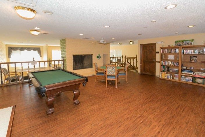 A spacious game room featuring a pool table and seating area, with bookshelves along the wall.