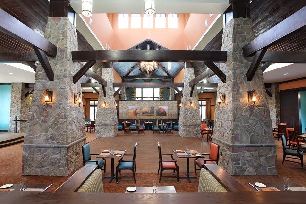 A spacious restaurant interior featuring stone pillars, wooden beams, and elegant chandeliers.