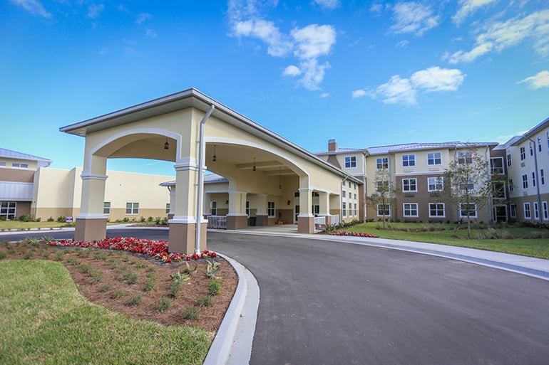 A modern building with a covered entrance and landscaped driveway under a clear blue sky.