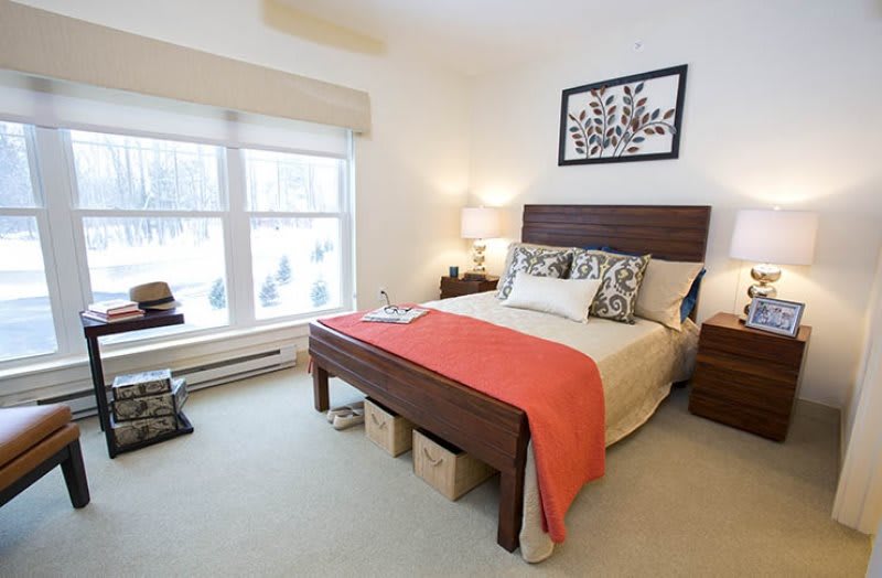 A modern bedroom with a neatly made bed, stylish decor, and natural light from a large window.