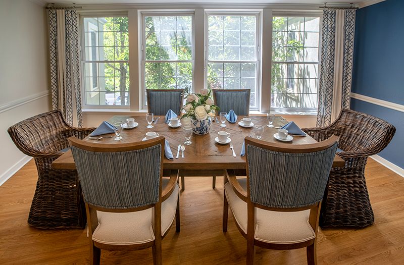 A beautifully set dining table with blue napkins and a floral centerpiece, surrounded by upholstered chairs in a well-lit room.