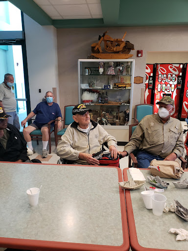 A group of individuals gathered indoors, some wearing masks, engaged in conversation.