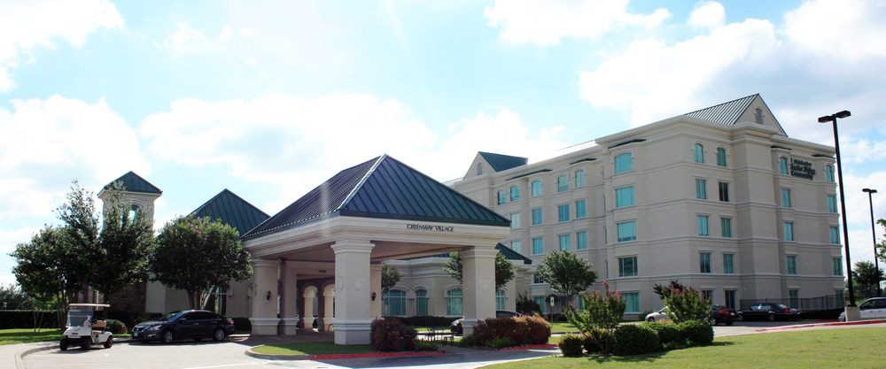 A modern hotel building with an inviting entrance and landscaped surroundings under a clear sky.