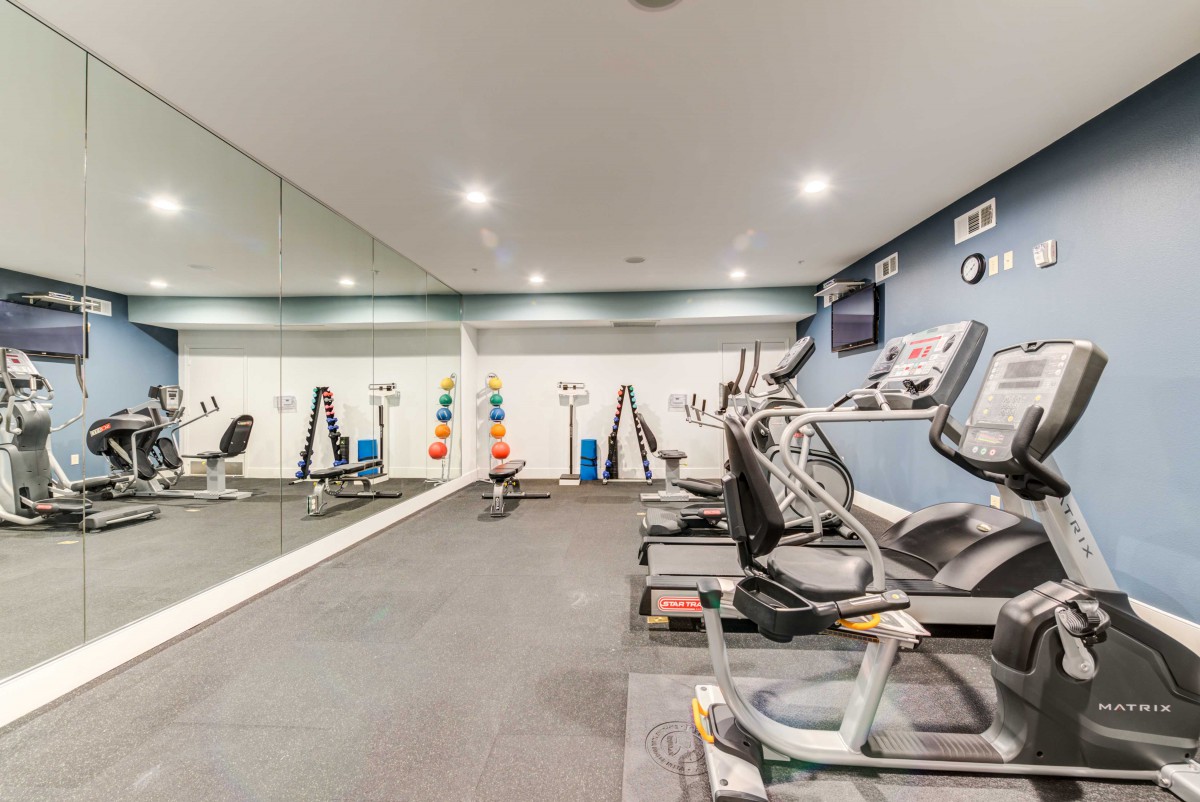 A well-equipped indoor gym with treadmills, elliptical machines, and mirrors.