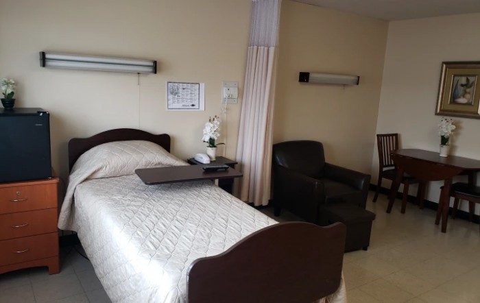 A hospital room with a bed, chair, and bedside table.