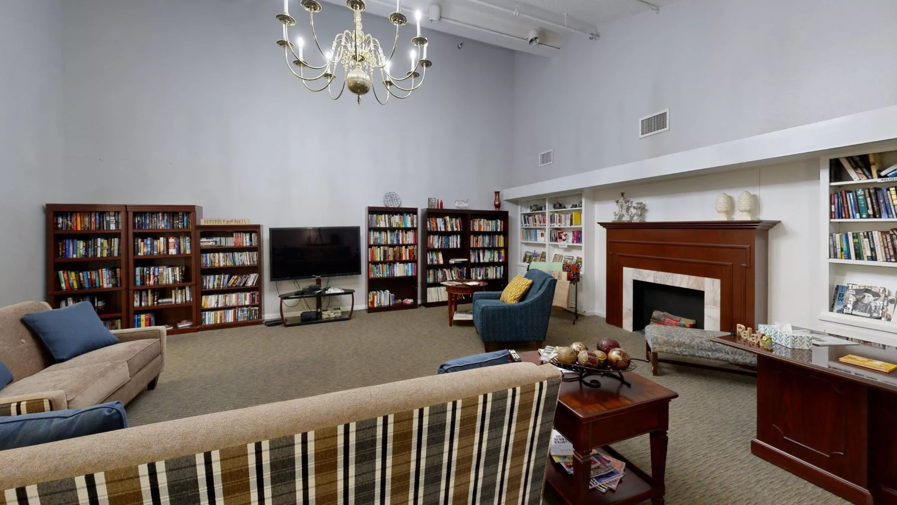 A cozy living room with bookshelves, a TV, an armchair, and a fireplace.