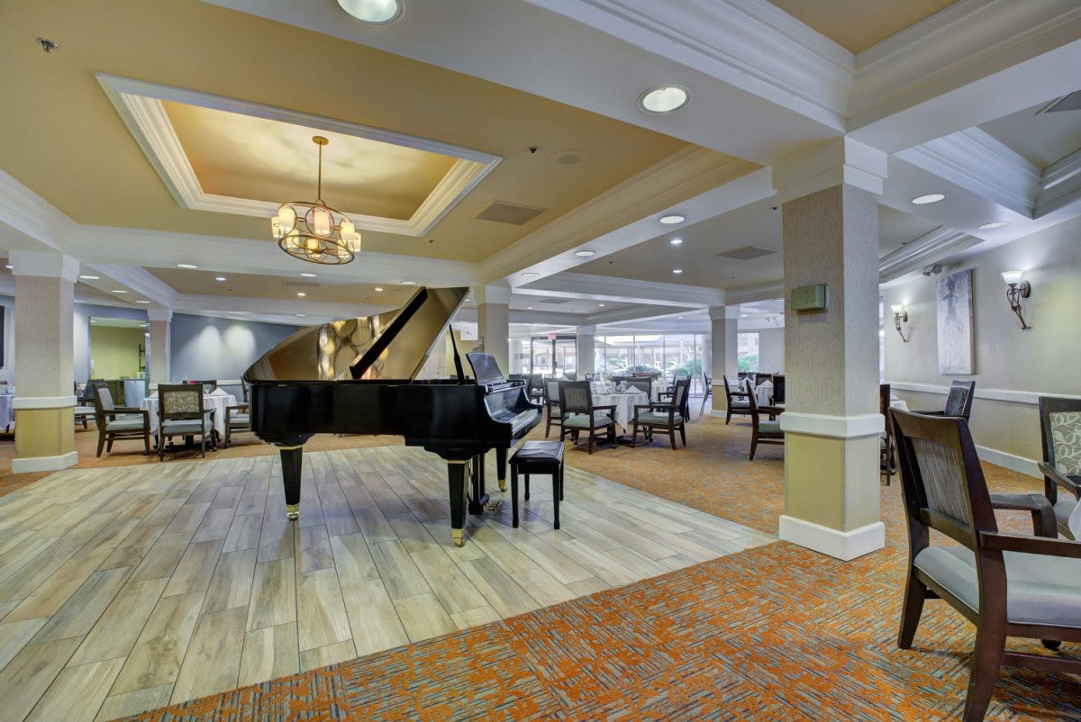 A spacious and elegant lounge featuring a grand piano and dining area with a chandelier.
