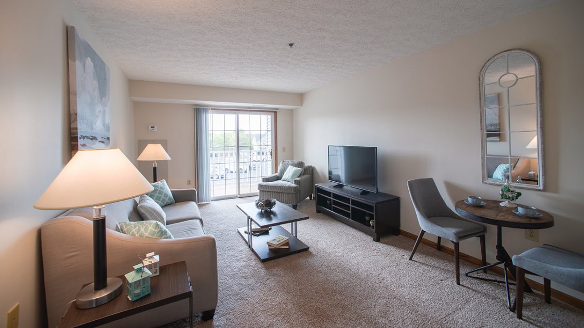 A cozy living room with modern furniture and a large television, featuring a sliding glass door that lets in natural light.