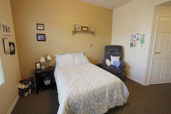 A cozy bedroom with a neatly made bed, an armchair, and decorative elements on the wall.
