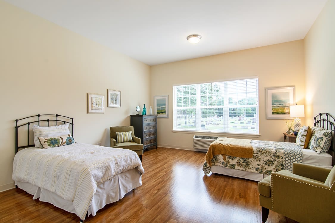 A bright bedroom with two twin beds, wooden flooring, and a large window letting in natural light.