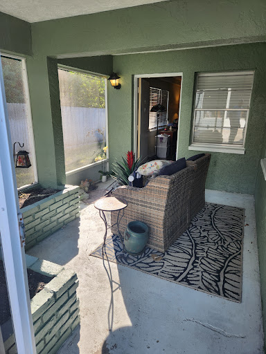 A cozy outdoor porch setup with comfortable seating and decorative plants, framed by green walls and natural light.
