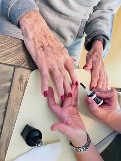 A person applies red nail polish to the fingernails of an elderly individual.