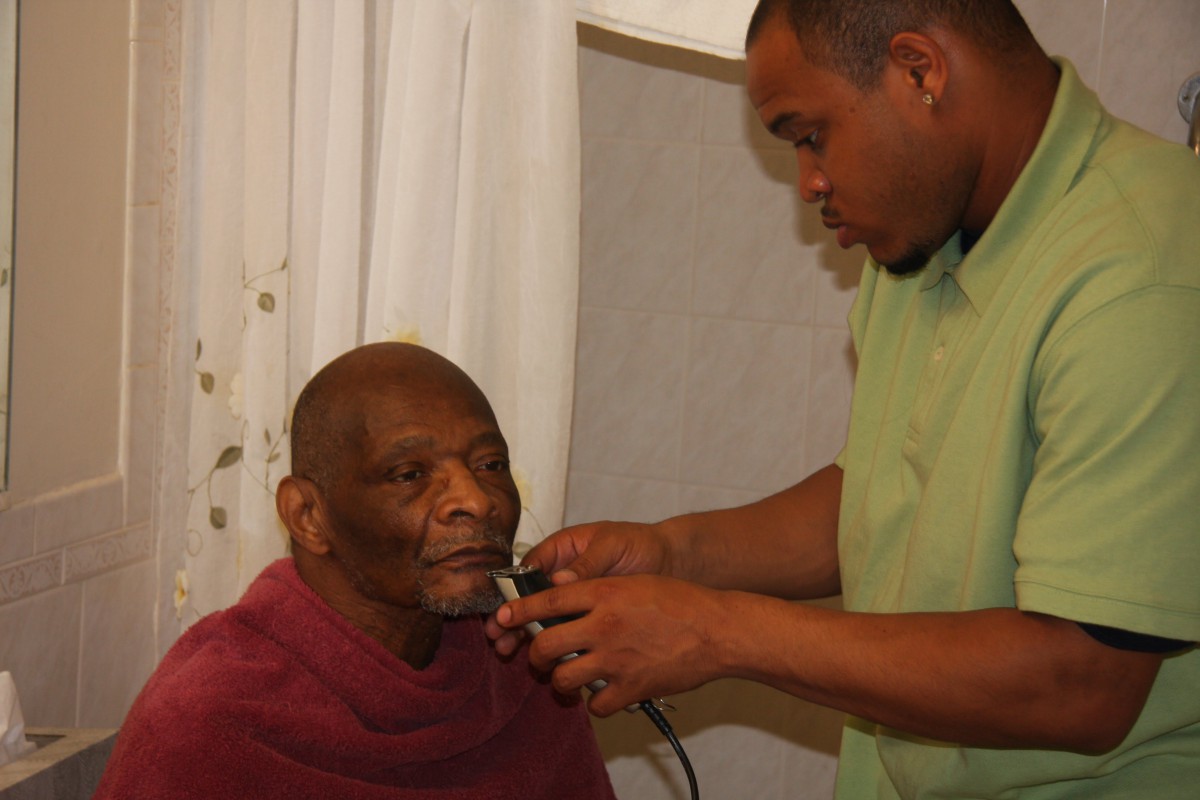 A caregiver providing grooming services to an elderly man.