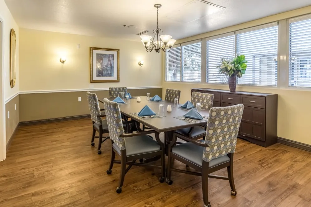A beautifully set dining room with a large table and elegant chairs, featuring a chandelier and window views.