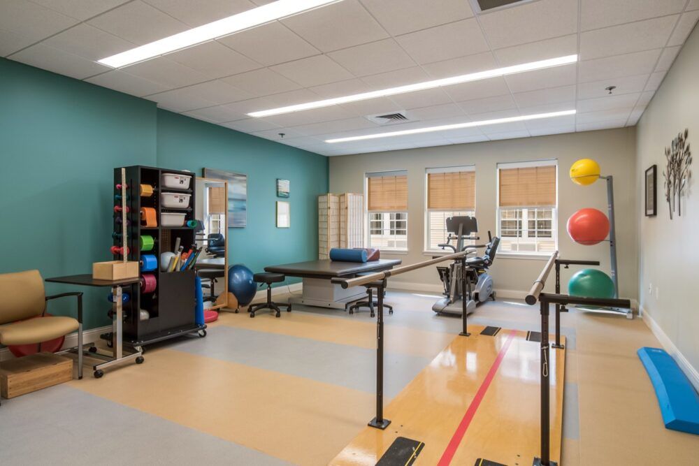 A rehabilitation room equipped with therapy tables, fitness balls, and parallel bars for physical therapy exercises.