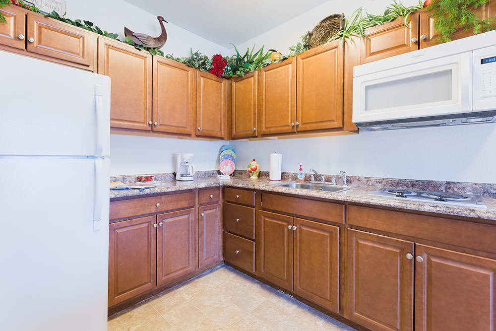 A cozy kitchen with wooden cabinets, a microwave, and decorative plants on top of the cabinets.