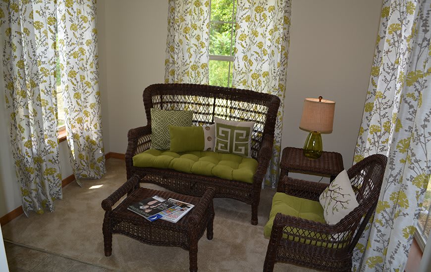 A cozy living room with wicker furniture and green cushions, featuring a sofa, coffee table, and armchair.
