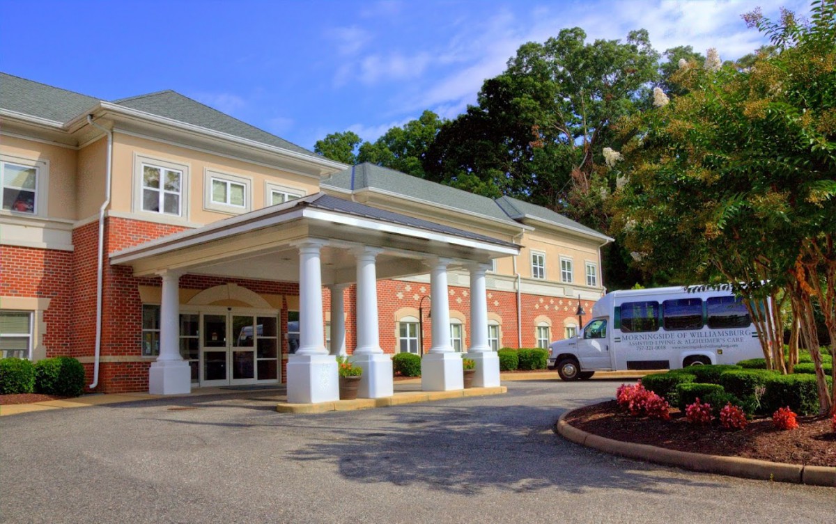 A building entrance with a portico and columns, surrounded by trees and with a van parked nearby.