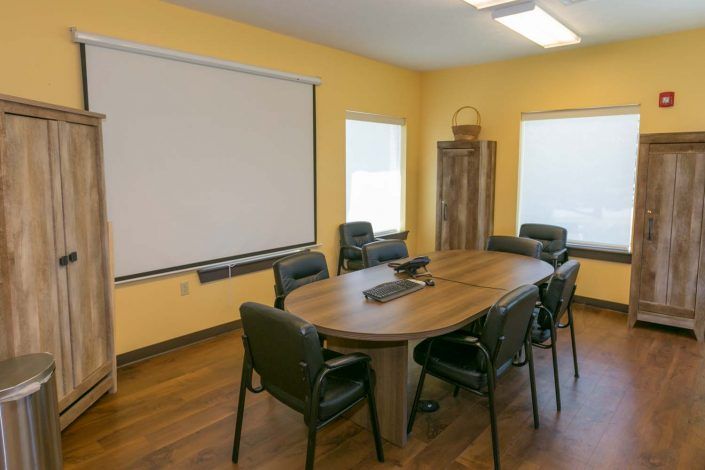 A well-organized conference room equipped with a large table, chairs, and a projector screen.