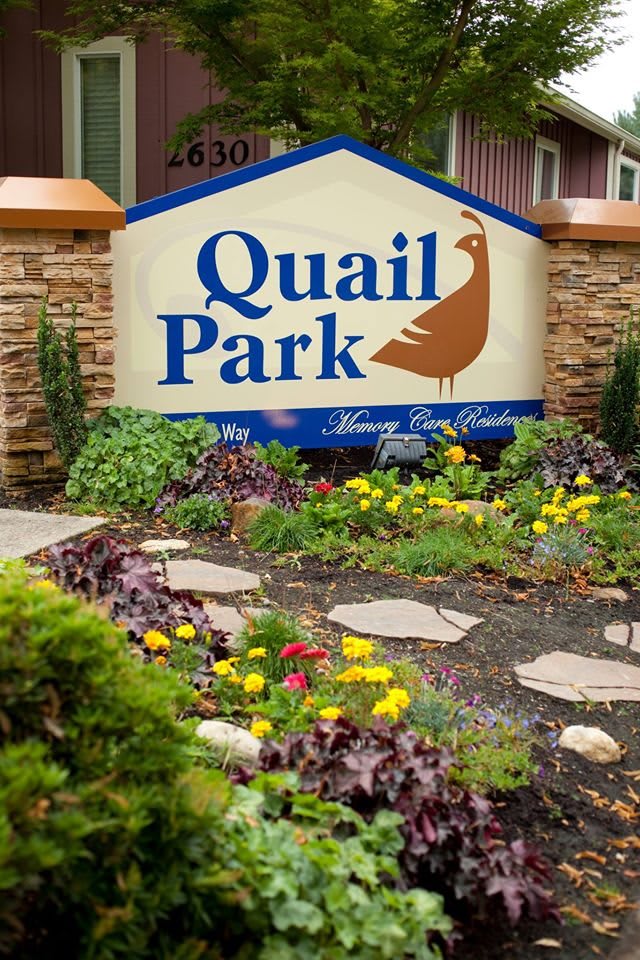 A landscaped garden with a 'Quail Park' sign surrounded by vibrant flowers.