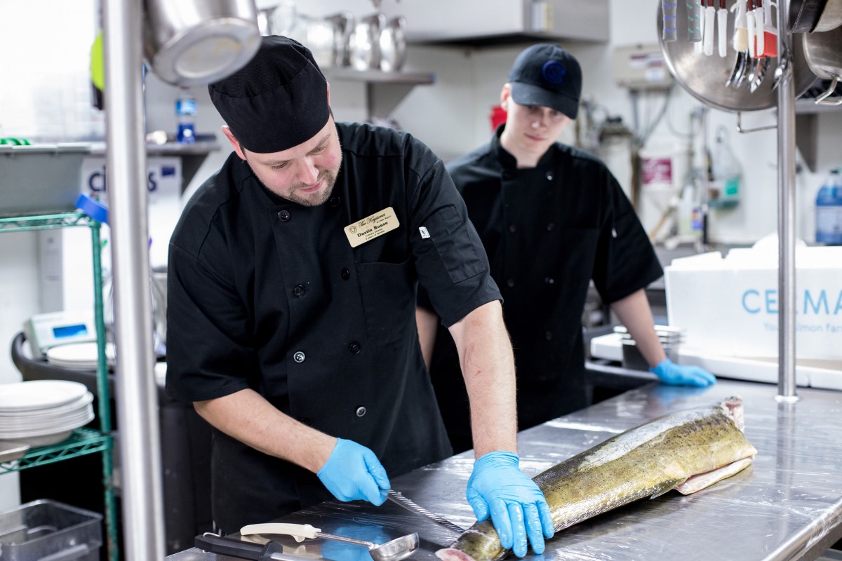 Chefs preparing fish in a professional kitchen.