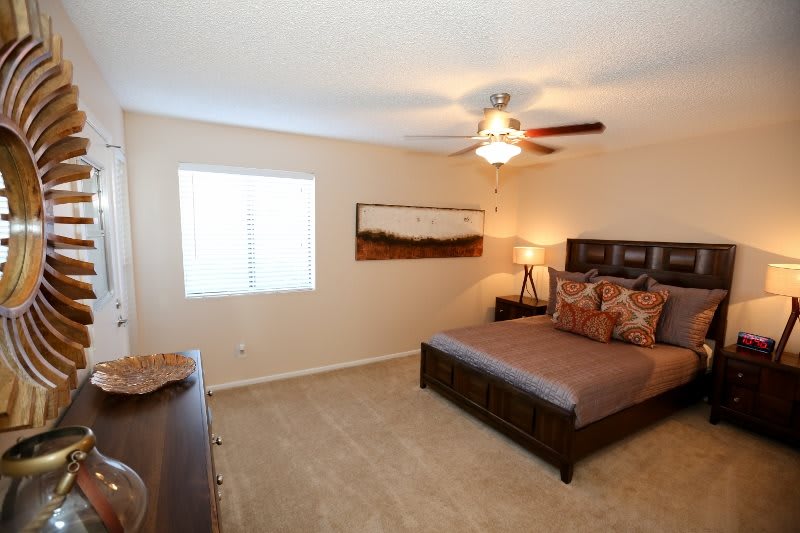 A cozy bedroom with a modern design, featuring a bed, nightstands, and a ceiling fan.