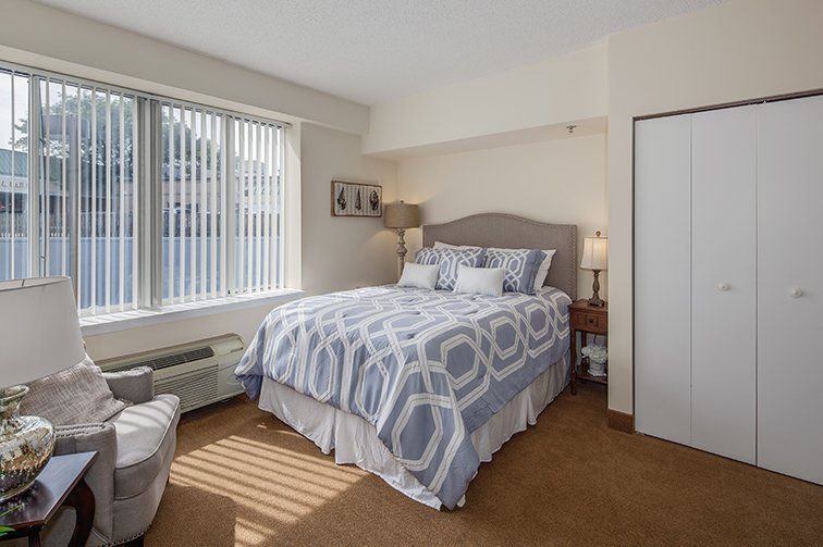 A cozy bedroom with a neatly made bed, soft lighting, and a large window.