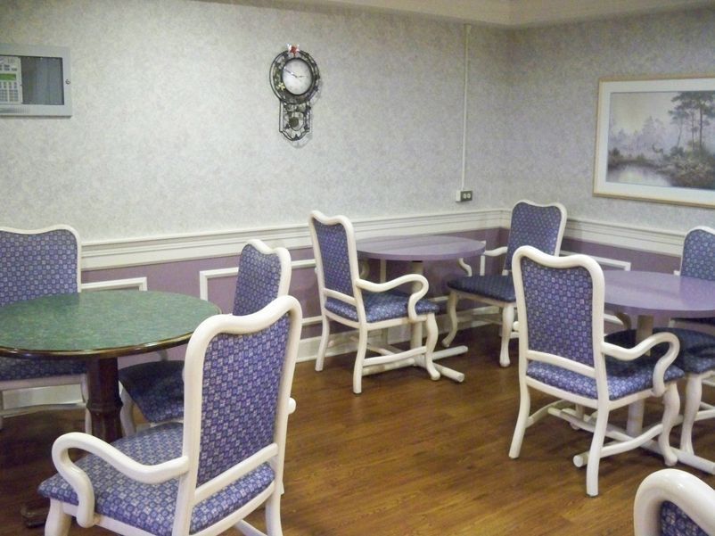 A cozy dining area with blue upholstered chairs and wooden tables, adorned with a decorative wall clock.