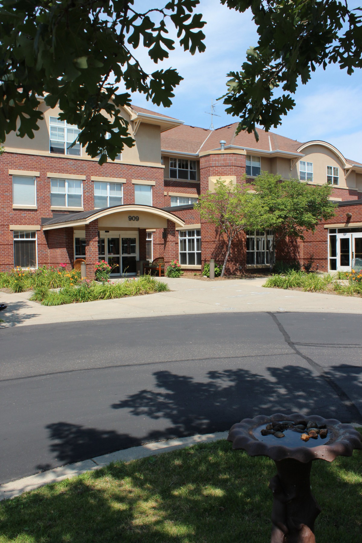 A brick building with an arched entrance surrounded by greenery and adjacent to a paved road.