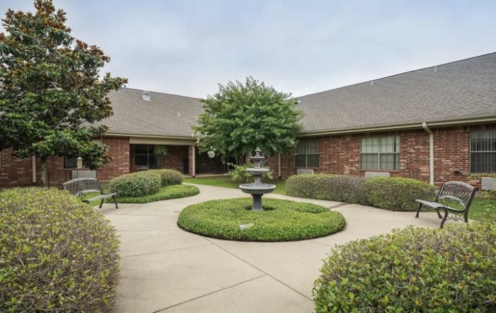 A serene courtyard with a central fountain, surrounded by lush greenery and brick buildings.