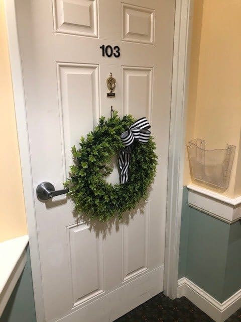 A door with the number 103 is decorated with a green wreath and black-and-white striped bow.
