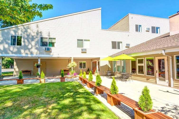A modern home with a spacious backyard and patio area, featuring outdoor seating and lush landscaping on a sunny day.