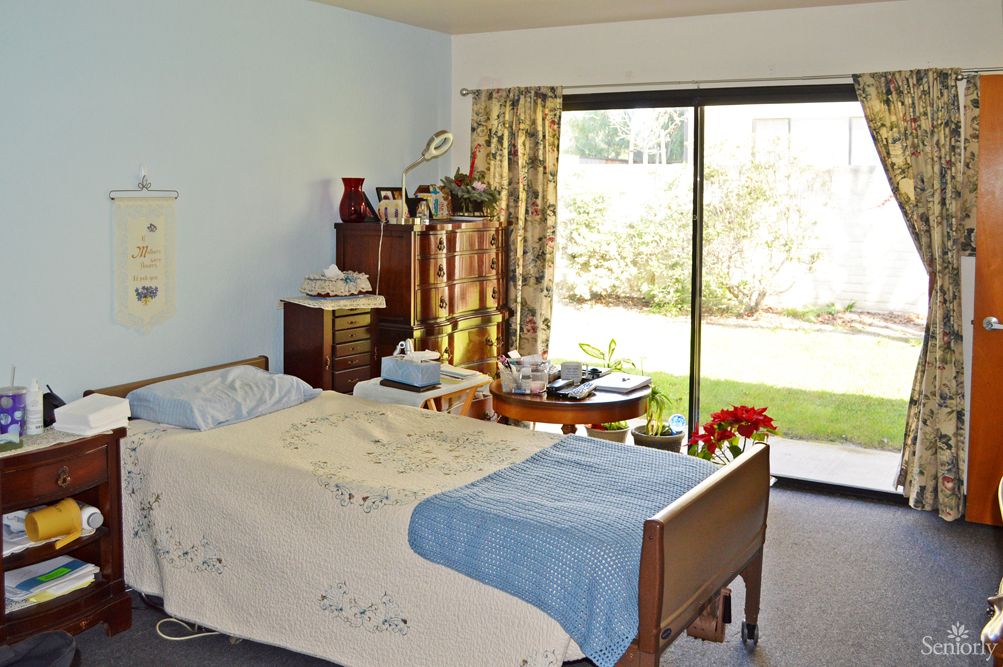 A bedroom featuring a hospital bed, wooden furniture, and a sliding glass door leading to a garden.