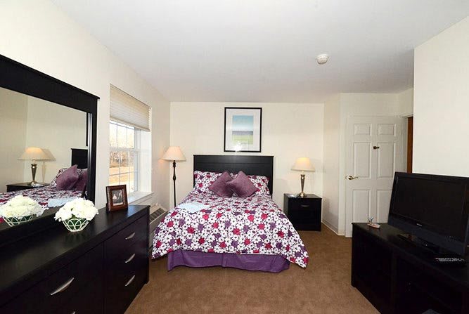 A cozy bedroom with a floral bedspread, two lamps, and a dresser with a mirror.