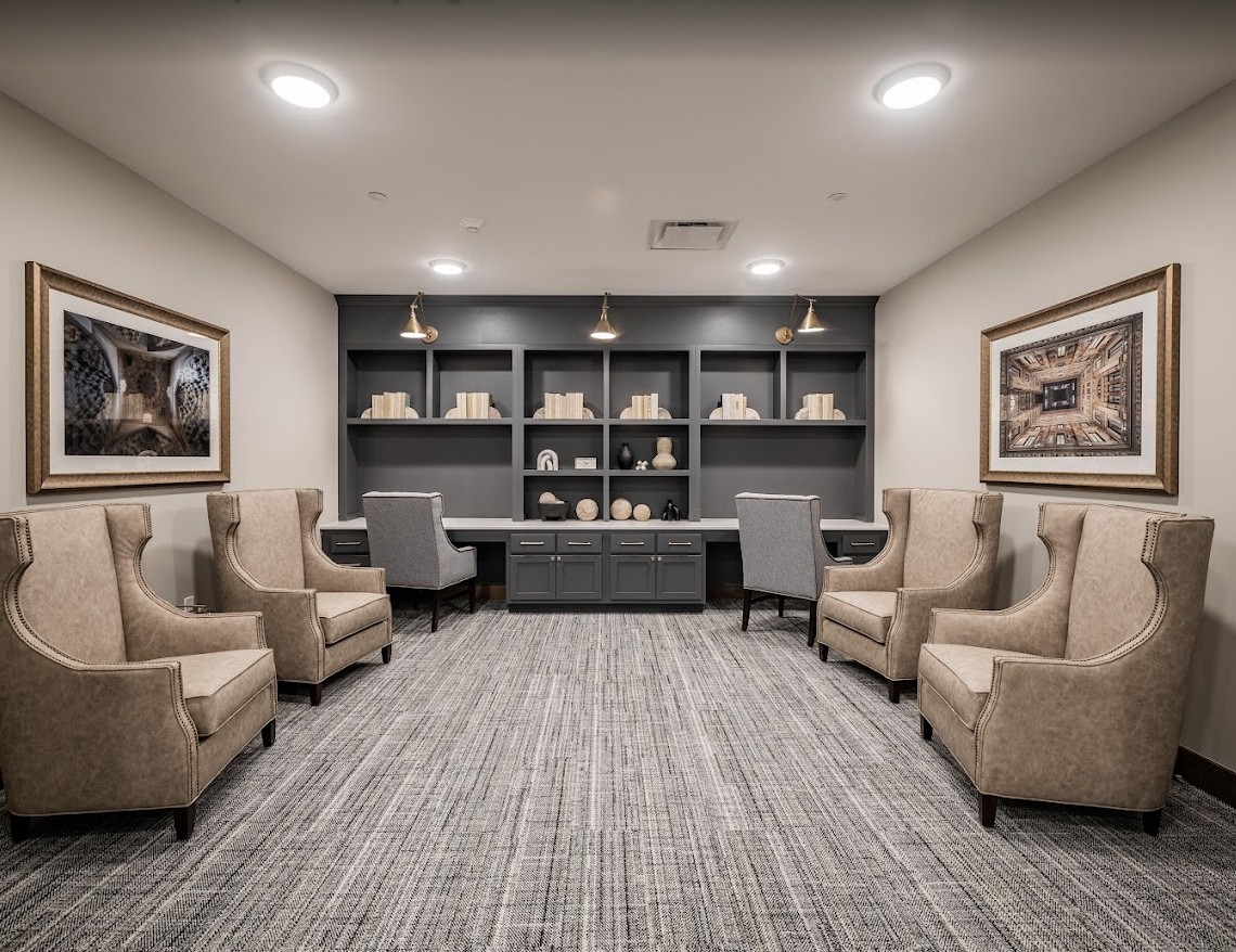 A modern office lounge with comfortable seating and bookshelves, decorated with framed artwork.