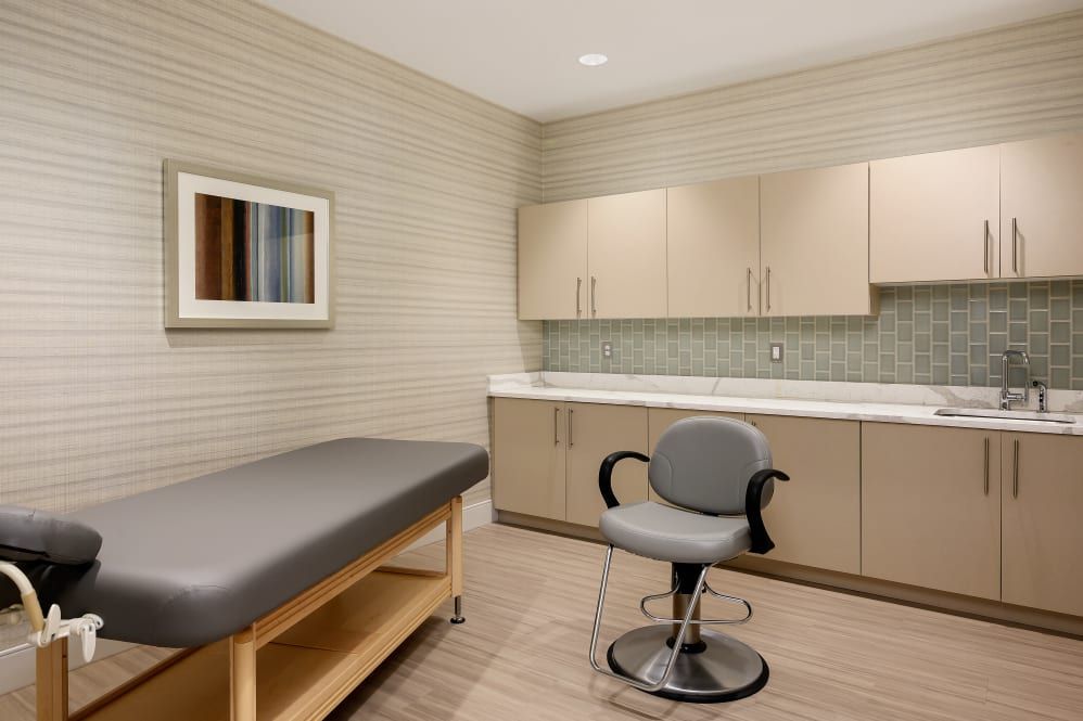 A clean and modern medical examination room with an examination table, chair, and cabinets.