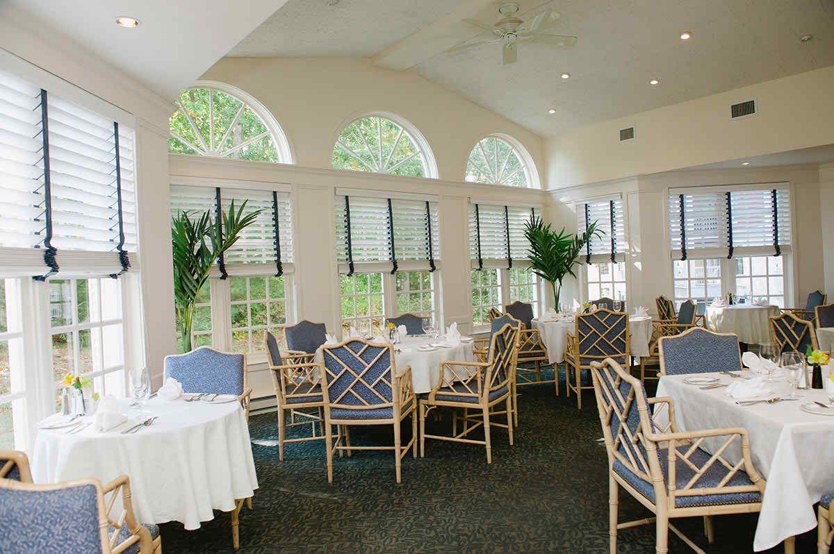 A bright and elegant restaurant dining area with neatly arranged tables and chairs, enhanced by natural light and greenery.