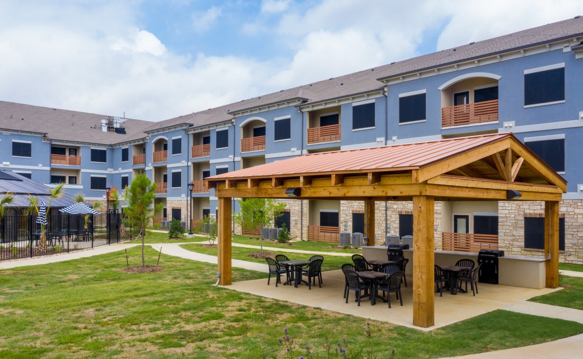 A modern apartment complex with an outdoor seating area featuring a wooden pergola.
