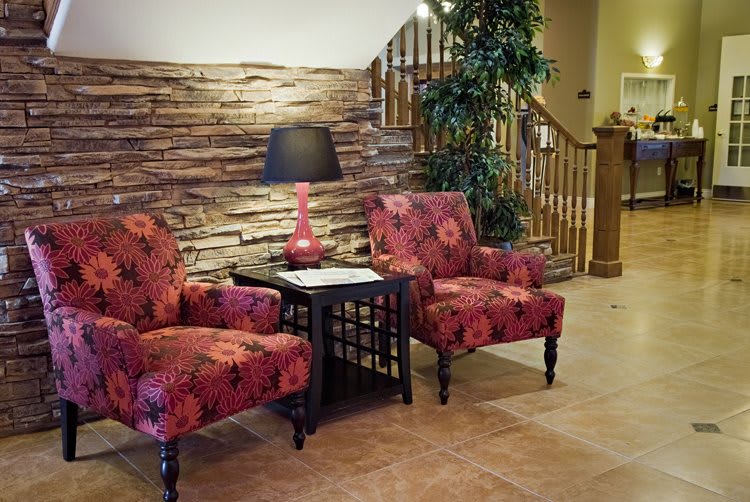 A cozy living room with two patterned armchairs, a lamp on a side table, and a staircase in the background.