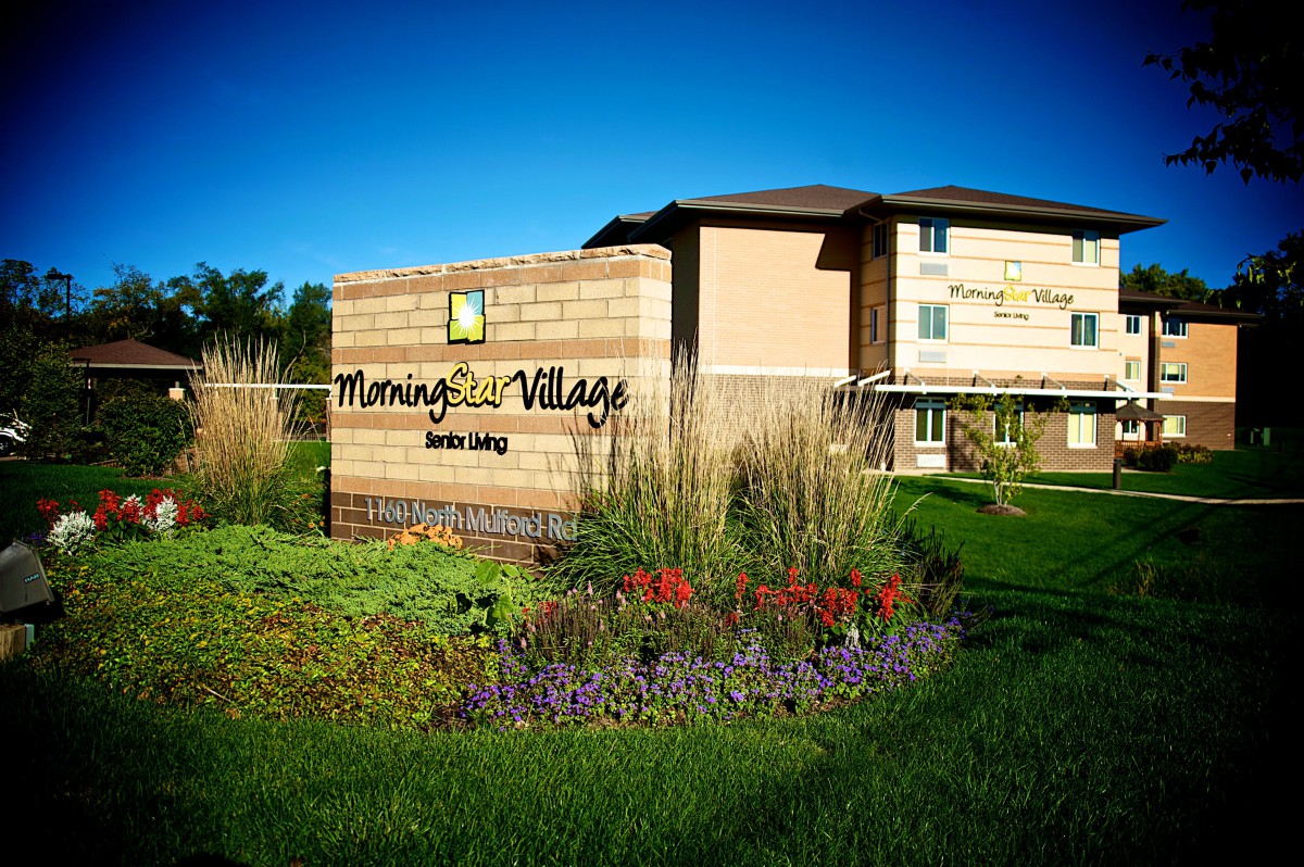 A well-maintained apartment complex with lush landscaping and a prominent sign in front.