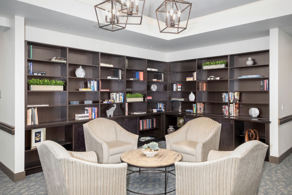 A cozy library corner featuring modern armchairs and extensive bookshelves under stylish lighting.