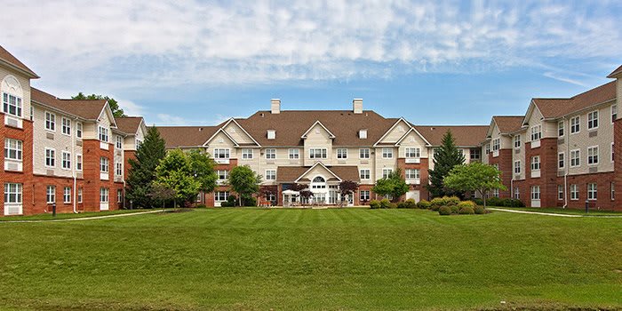 A large residential building with a spacious lawn and trees under a partly cloudy sky.