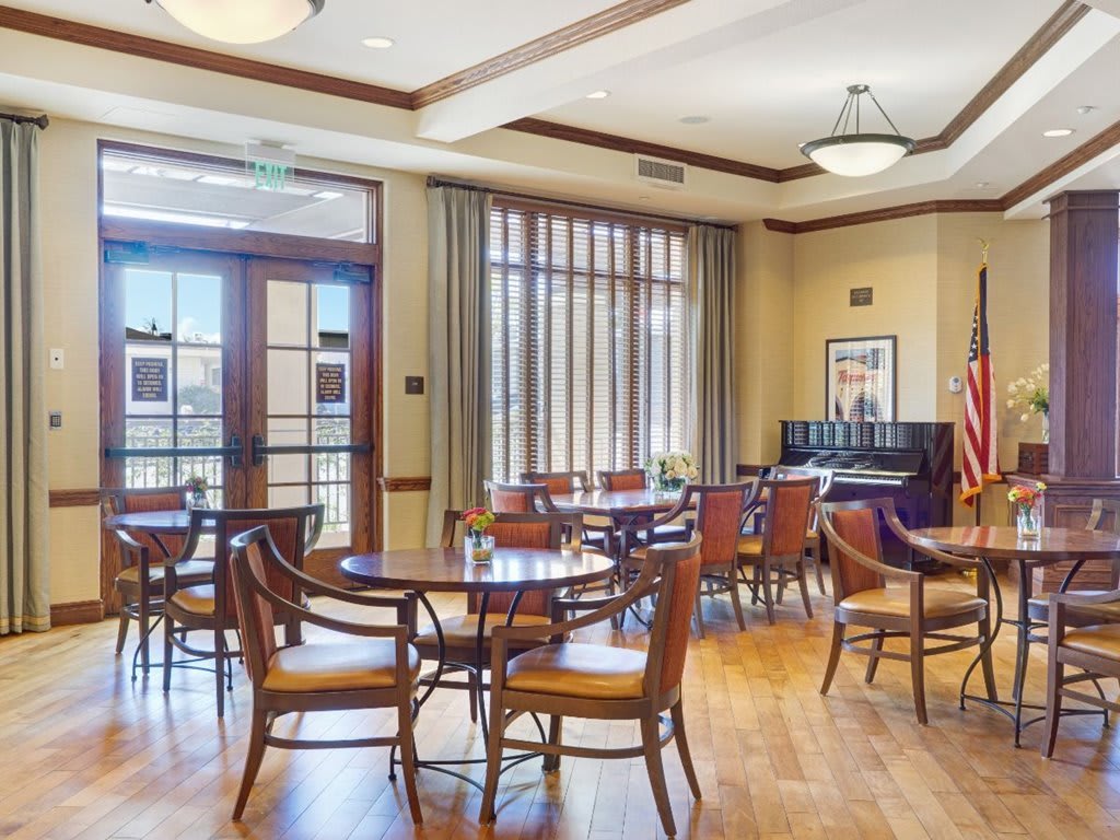 A well-lit room with wooden floors, featuring tables and chairs arranged for a meeting or gathering.