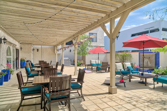 A spacious outdoor patio with comfortable seating under a wooden pergola, featuring tables, chairs, and colorful umbrellas.