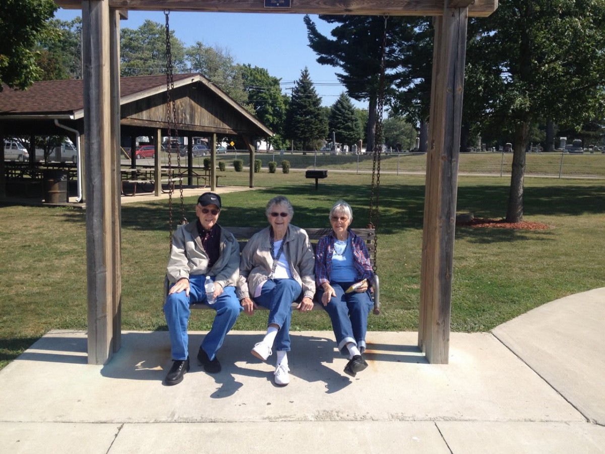 Three people sitting on a swing in a park setting.
