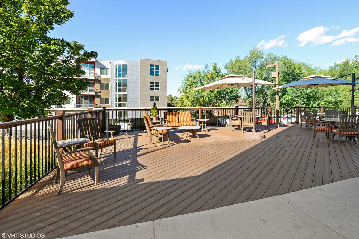 A spacious outdoor patio area with seating and umbrellas, adjacent to apartment buildings on a sunny day.