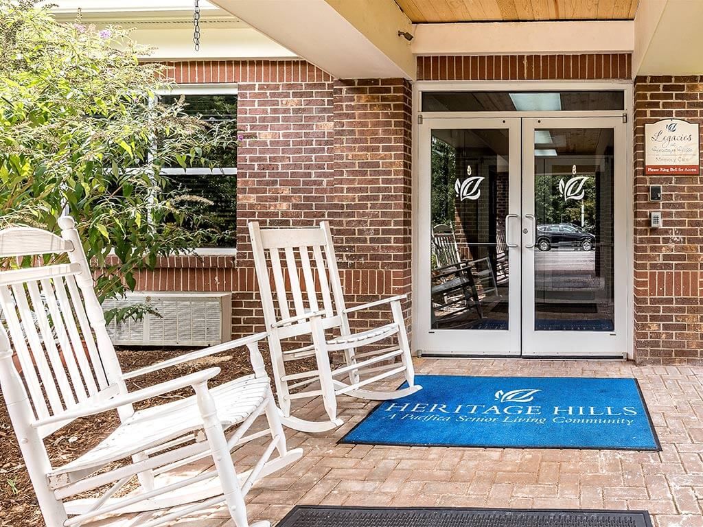 A welcoming entrance with white rocking chairs and a blue welcome mat.