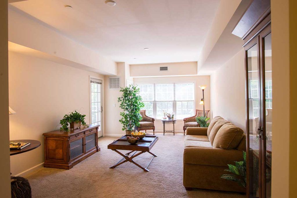 A cozy living room with a sofa set, coffee table, and plants near a large window.