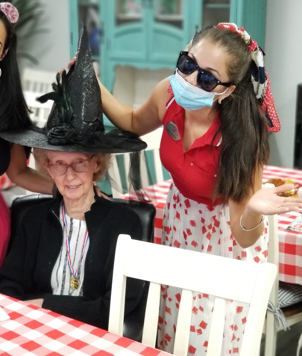 A person in a witch hat at a festive gathering with others dressed up for Halloween.