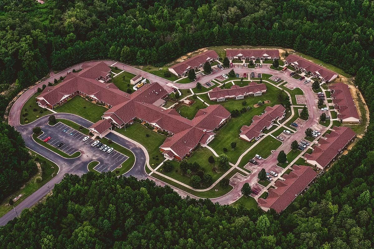 Aerial view of a large complex with red-roofed buildings surrounded by greenery and connected by roads.